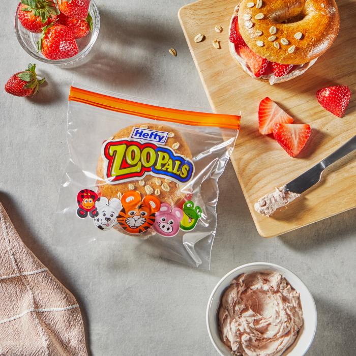 Bagel topped with cream cheese and sliced strawberries in a Hefty Zoo Pals sandwich bag sitting on a kitchen counter