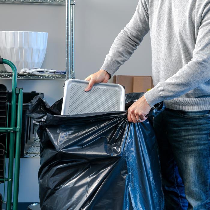 person stuffing a paint tray into a Hefty contractor bag