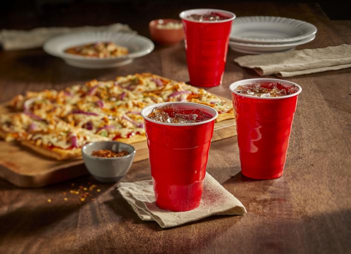 Hefty 18oz red party cups filled with cola sitting on a kitchen table alongside a pizza