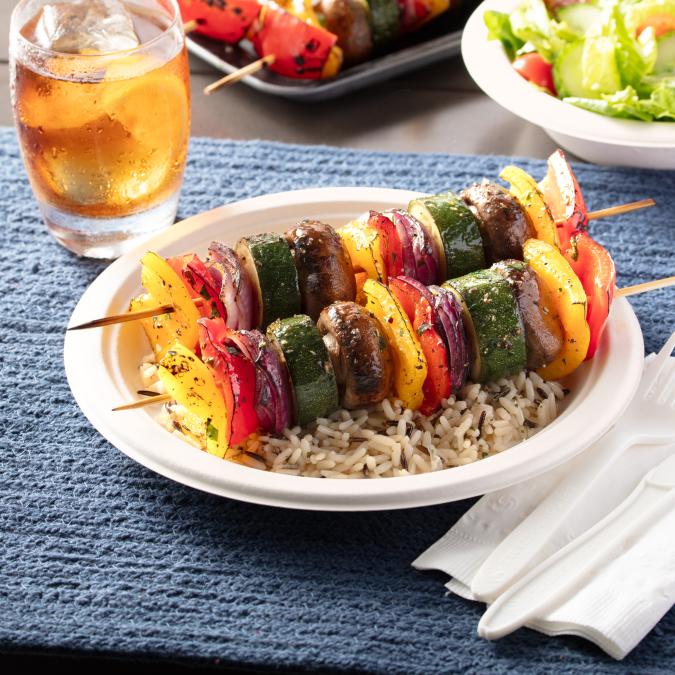 Vegetable kabobs sitting on a bed of rice on a 9" Hefty ECOSAVE plate on an outdoor table