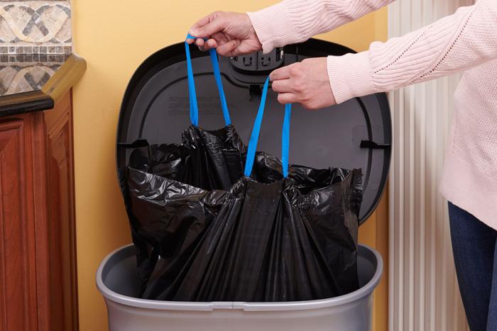 Person closing a strong drawstring large bag in a trash can.