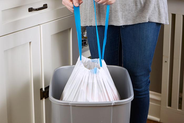 Person pulling an ultra strong drawstring kitchen trash bag out of a trash can.