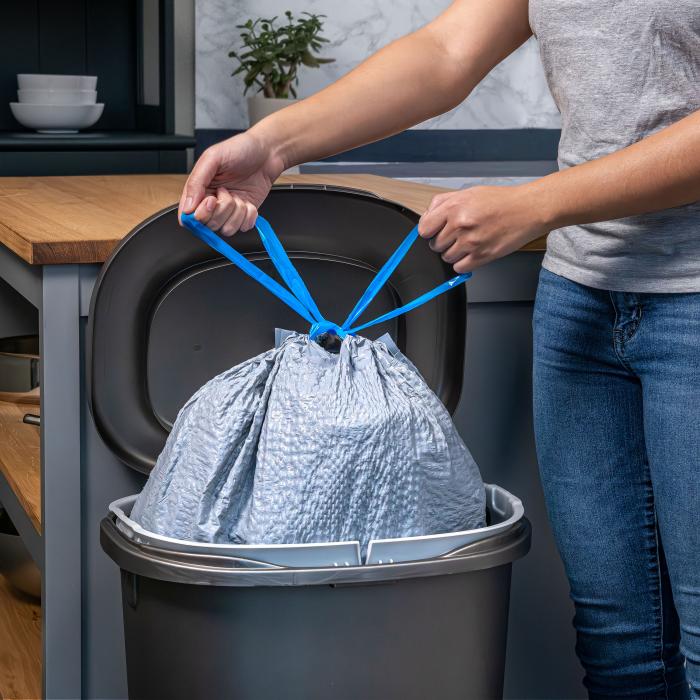 Person tying the drawstrings of a trash bag and pulling it out of the garbage can