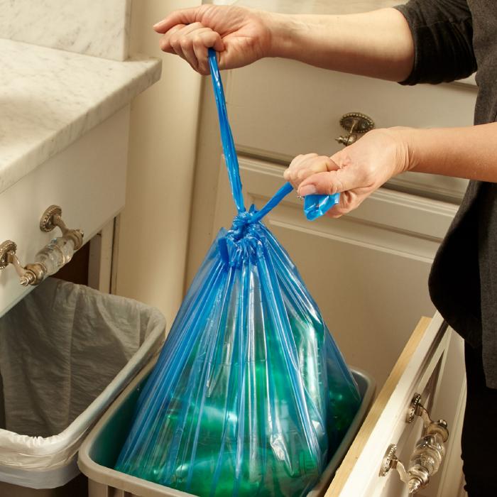 Person pulling a tied blue bag from the trash can