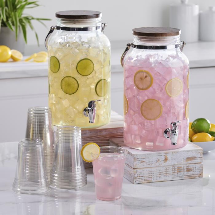 Beverage dispensers filled with lemonade sitting alongside a stack of clear disposable cups
