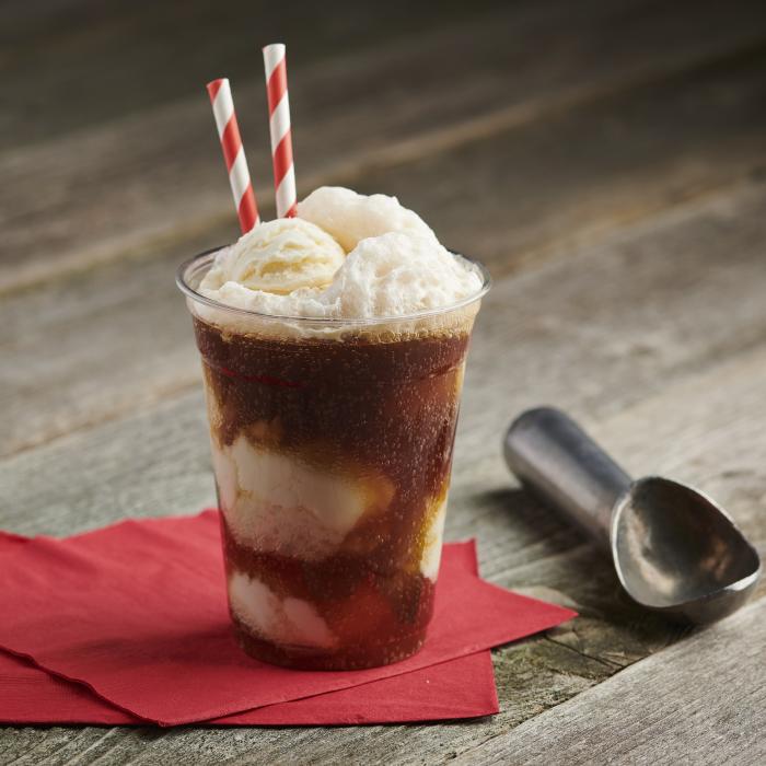 Root beer float sitting on a rustic wood background alongside an ice cream scooper