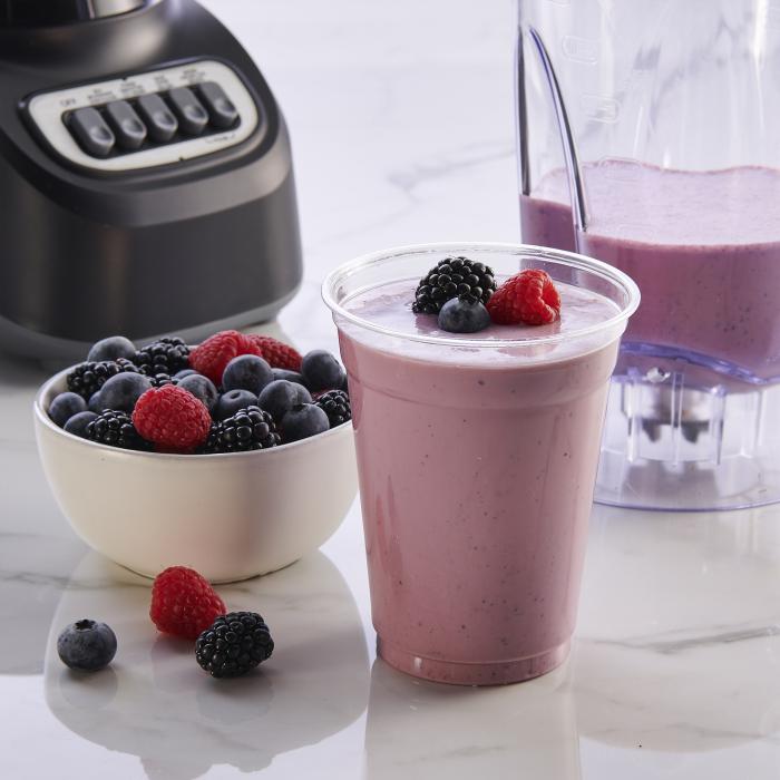 Berry smoothie sitting on a marble countertop alongside a blender and bowl of berries