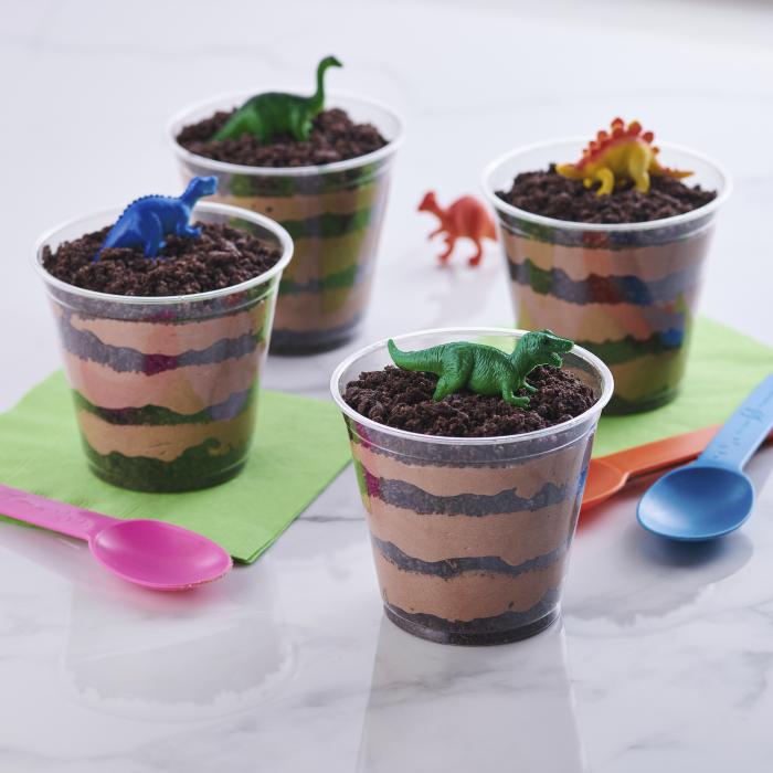 Chocolate pudding and Oreo dirt cup in clear plastic cups topped with dinosaurs 